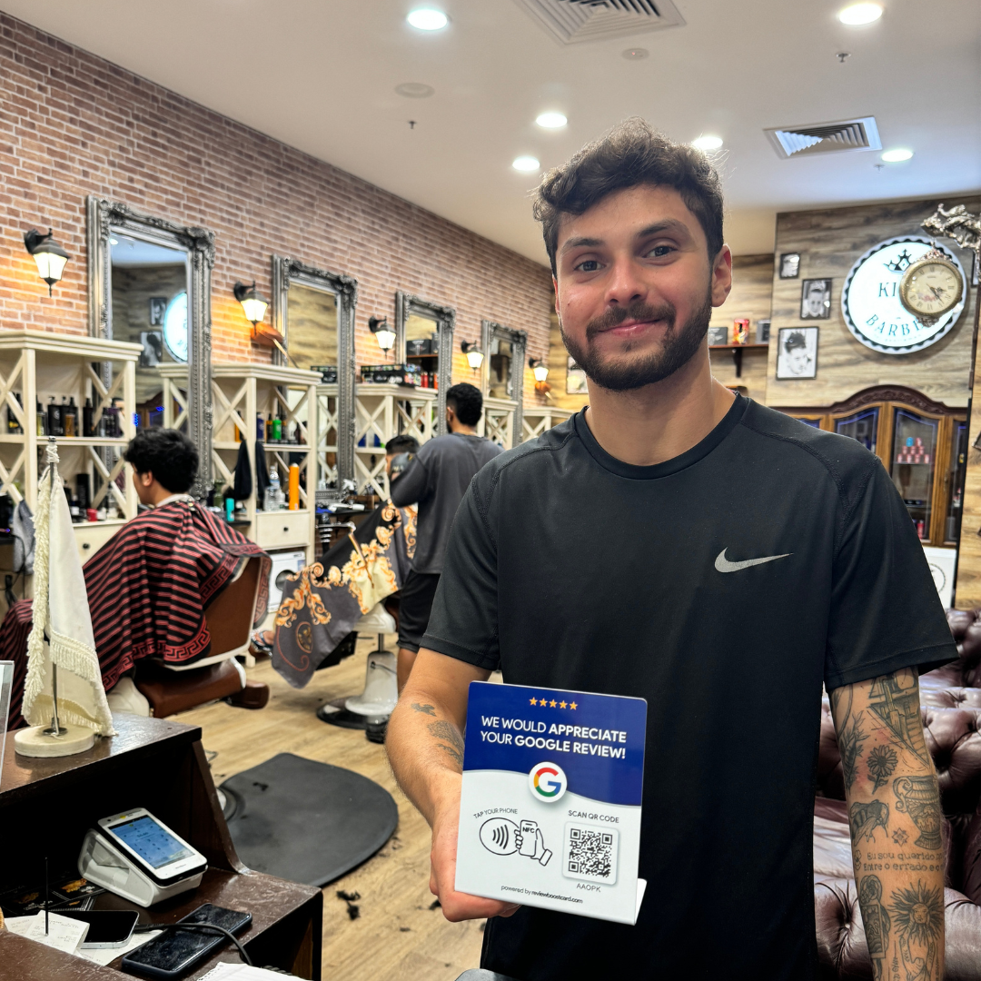 Barber shop owner proudly holding the ReviewBoost Google review stand, a sleek device designed to encourage customer feedback with an easy-to-use QR code display, helping to boost online reviews and visibility