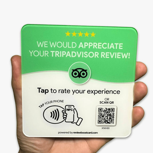 A hand holding a ReviewBoost card requesting a TripAdvisor review. The card is green and white with the TripAdvisor logo and text that says, 'We would appreciate your TripAdvisor review! Tap to rate your experience. Tap your phone or scan QR