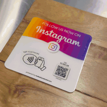 An animated GIF showing an Instagram follow plaque on a wooden surface. The plaque has a gradient from orange to purple, featuring the Instagram logo, with instructions to 